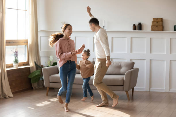 Couple dancing with little daughter barefoot in warm living room Cheery couple dancing with little daughter barefoot on wooden laminate floor with underfloor heating system in modern warm living room. New home, bank loan and lending, hobby and fun with kids concept barefoot stock pictures, royalty-free photos & images