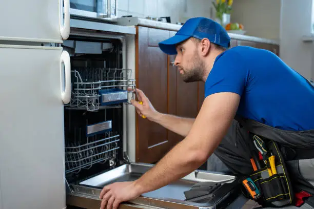 Repair of dishwashers. Repairman repairing dishwasher in kitchen.