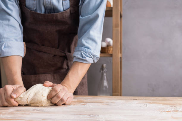 Baker man kneading or making dough and bakery ingredients for homemade bread cooking on shelf. Bakery concept