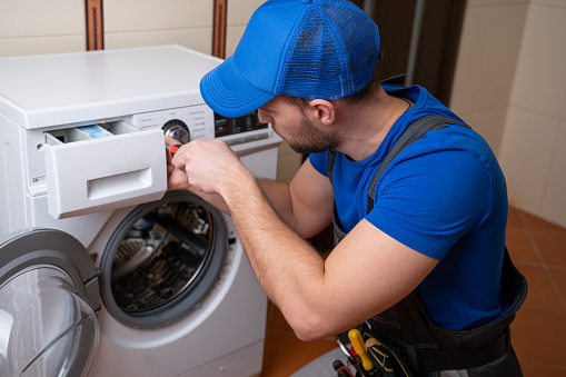 Worker repairing washing machine in laundry room.