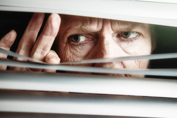 istock Elderly woman peering anxiously through window blinds 1309389232