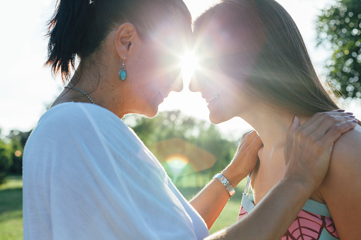 Cute pretty teen daughter with mature mother hugging in nature at sunset.