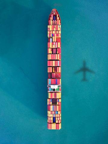 Airplane flying over container ship in the ocean.