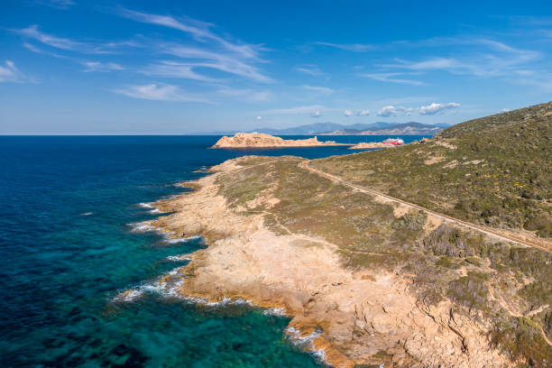 Ile Rousse, Corsica, France - 23rd March 2021. A Corsica Linea ferry waits in the harbour at Ile Rousse with the railway track winding along the rugged coast of Corsica in the foreground