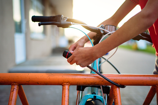 Girl teenager fastening bicycle lock on street parking at sunset