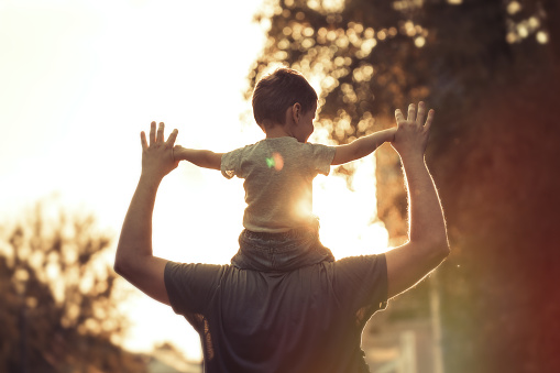 Father sitting and comforting sad son with autism, mental disorder and depression on garden step backyard patio. Back view of caring, loving and kind single parent supporting, comforting and talking