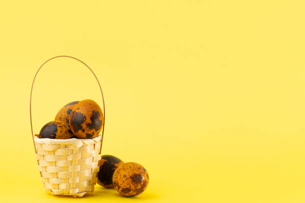 Easter colored orange quail eggs in a wicker basket and next to it on yellow background. Easter holiday concept. Copy space, close-up