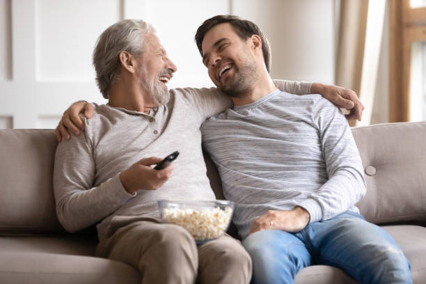 istock Happy older father with son hugging, watching tv at home 1309403982