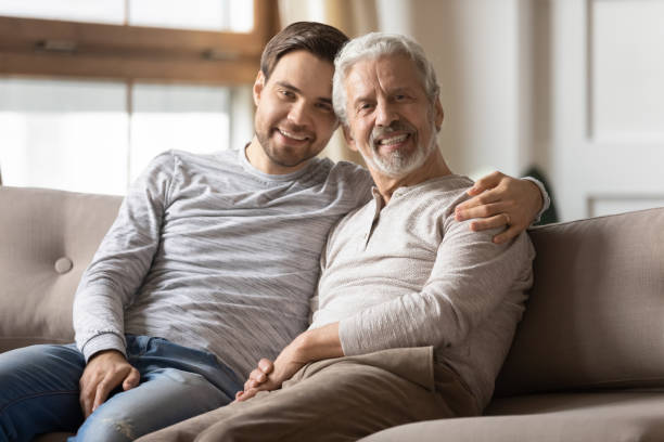 istock Portrait smiling young man hugging mature father, sitting on couch 1309404522