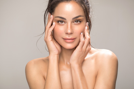 Close up studio shot of a beautiful brunette woman with glowing skin. Holding hands near her face.