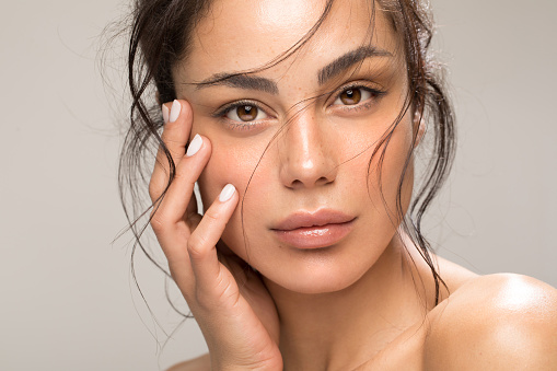Close up studio shot of a beautiful brunette woman with glowing skin. Holding hands near her face.