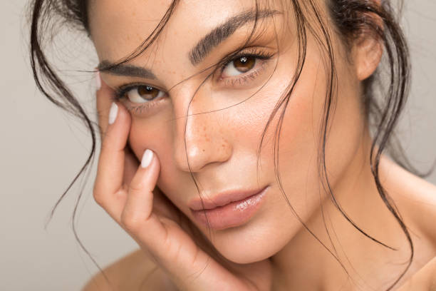 Beauty portrait of young brunette Close up studio shot of a beautiful brunette woman with glowing skin. Holding hands near her face. skin stock pictures, royalty-free photos & images