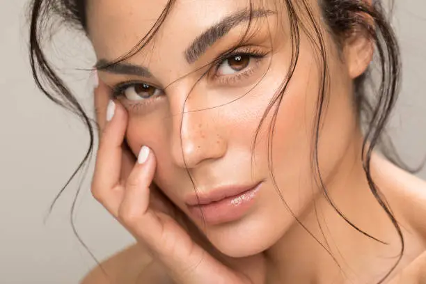 Close up studio shot of a beautiful brunette woman with glowing skin. Holding hands near her face.