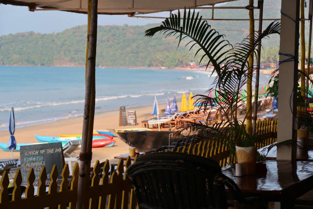 istock Image of restaurant tables and chairs ready for alfresco dining with beach view, overlooking parasols and loungers on Palolem Beach and Arabian Sea, Goa, South India 1309408429