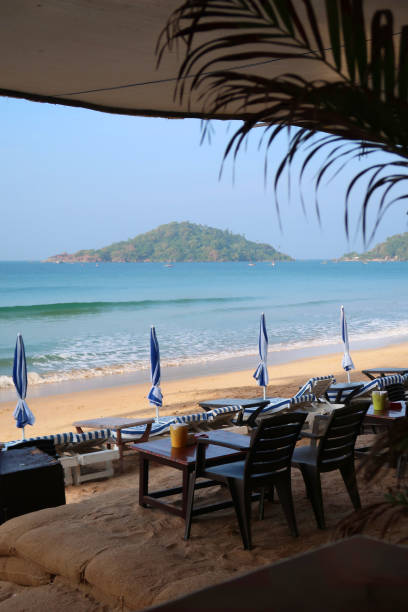 istock Image of restaurant tables and chairs ready for alfresco dining with beach view, overlooking parasols and loungers on Palolem Beach and Arabian Sea, Goa, South India 1309408963