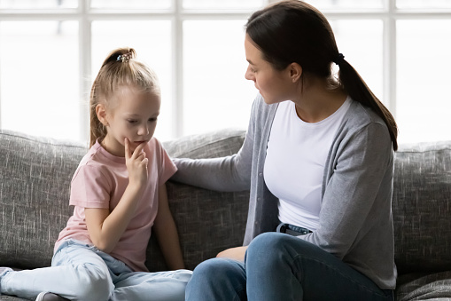 Serious mother talking to sad upset preschooler daughter kid at home. Mum consoling quiet girl, giving love, comfort, support, touching shoulder of child at home. Psychology, therapy,  empathy concept
