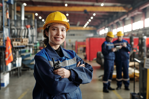 Joven trabajadora sonriente de planta industrial moderna o fábrica en ropa de trabajo y casco protector photo