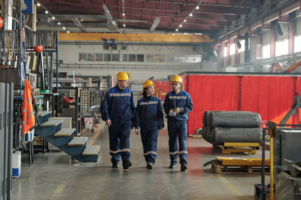 istock Three engineers moving along large workshop with industrial equipment and having conversation 1309413039