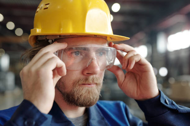 istock Young serious engineer or factory worker in protective helmet and eyeglasses standing in workshop 1309413060