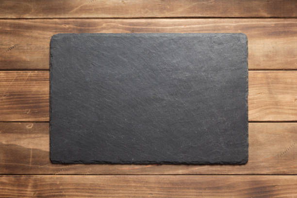 istock Black slate stone on wooden table board. Slate stone background texture 1309413271