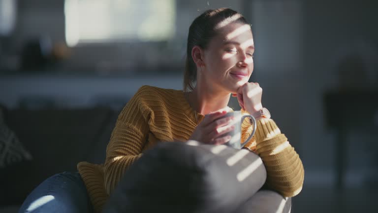 4k video footage of a young woman having a relaxing coffee break on the sofa at home