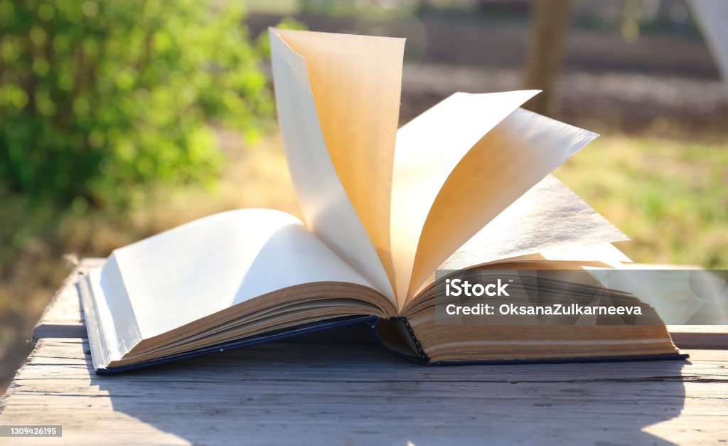 The book turns over outside Open old book on a wooden board and a background of greenery. The wind is turning pages. Reading and knowledge. Information and its meaning. Page Stock Photo