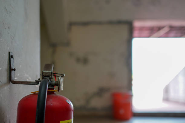 istock Close-up on fire fighting equipment in modern building. Old rusty fire extinguisher hangs on the wall. The blurred background is an orange trash can. 1309429749