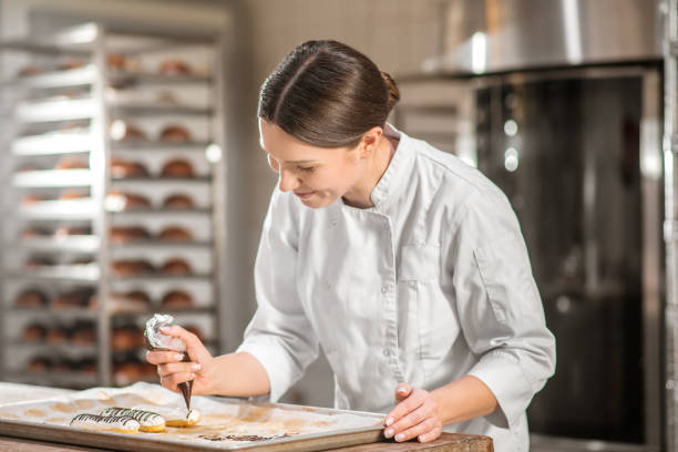 frau mit teigtasche über tablett mit kuchen - konditor stock-fotos und bilder