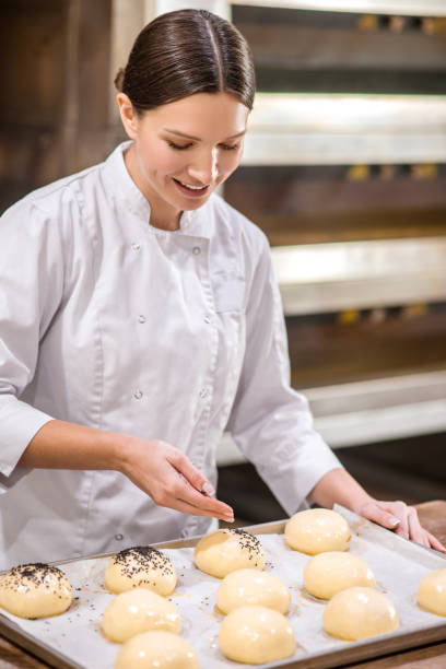 istock Woman sprinkling seeds on buns before baking 1309431402