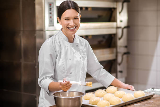 femme de sourire dans l’uniforme préparant des pains pour la cuisson - pâtissier photos et images de collection