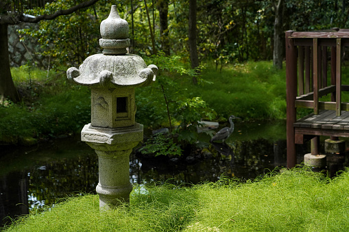 Japanese traditional lantern near small river or canal in Japanese garden,egret bird on background with old terrace nearby in Japan.