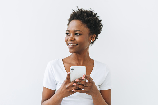 Smiling beautiful young African American woman in white T-shirt using mobile phone isolated on white background