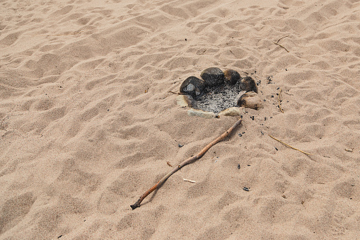 A fire pit on a sandy beach and a stick. Outdoor recreation. Wild vacation. Primitive people. Primitive life.