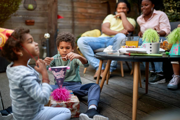 afro-american kids playing on a birthday party with their parents in the background. Family concept afro-american kids playing on a birthday party with their parents sitting in the background. Family concept happy birthday cousin images stock pictures, royalty-free photos & images
