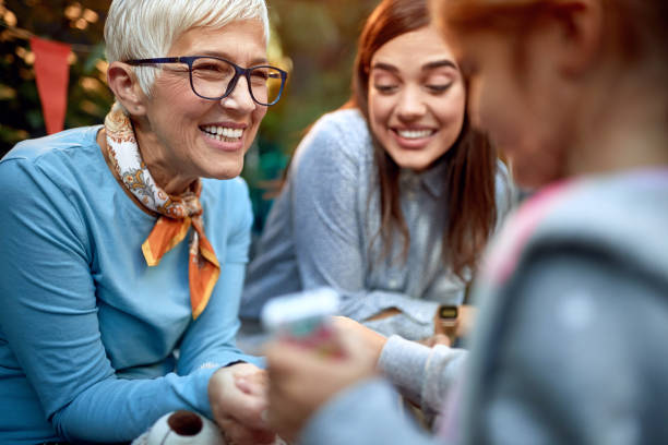 concepto de tres generaciones, niña recibiendo un regalo de su abuela con la madre mirando. - senior women grandmother glasses senior adult fotografías e imágenes de stock