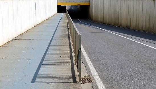 Two lane road with a pedestrian and cycle path next to it separated by a railing. An underpass in front and high concrete walls to the sides. Background for copy space
