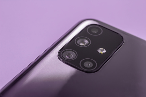 A modern smartphone with multiple camera lenses and a built-in flash close-up on a lilac background. The selected focus.