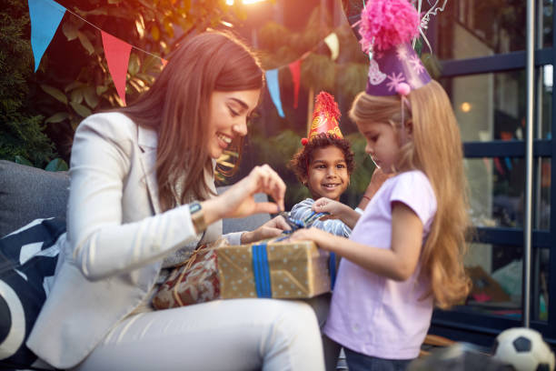 beautiful young female adult opening birthday present with a little gir beautiful young female adult opening birthday present with a little girl with a friend in the background happy birthday cousin images stock pictures, royalty-free photos & images