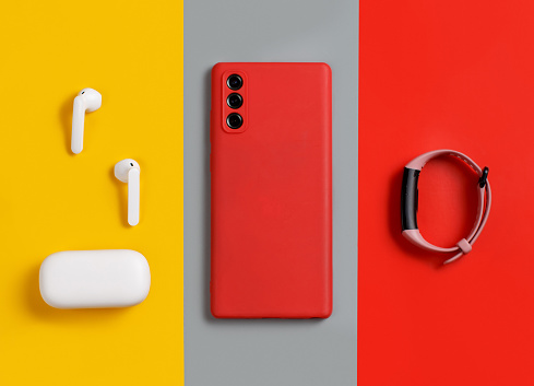 Smartphone, white wireless earphones awith the case and  smart watch top view on red, grey and yellow background