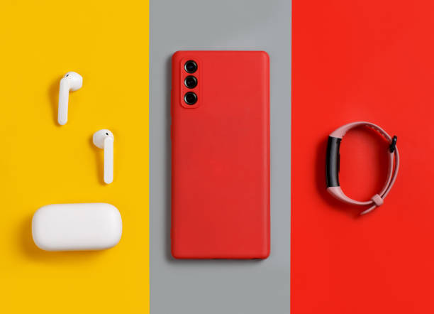 Smartphone, white wireless earphones and smart watch Smartphone, white wireless earphones awith the case and  smart watch top view on red, grey and yellow background in ear headphones stock pictures, royalty-free photos & images