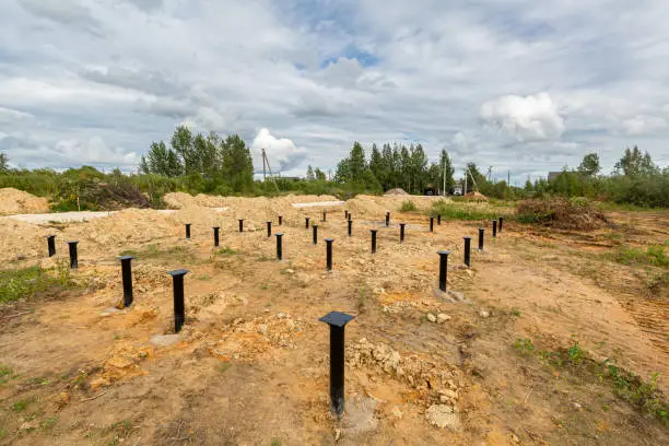 Photo of Iron screw piles in the ground for a new building on construction site.