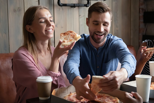 Tastes great! Happy excited young male and female loving couple mates colleagues spending good time at favorite pizzeria with group of friends on weekend having fun enjoying pizza laughing chatting