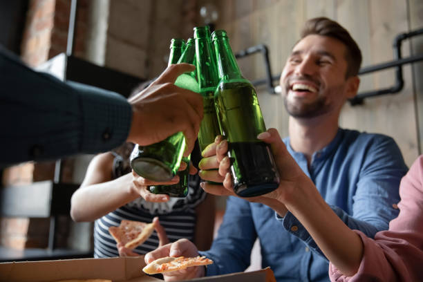 diversos amigos do milênio fazendo brindes para reunião levantando garrafas de cerveja - green beer fotos - fotografias e filmes do acervo