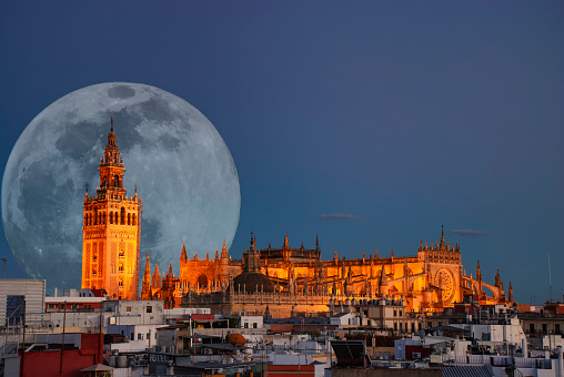 A full moon behind the illuminated cathedral in Seville, Spain