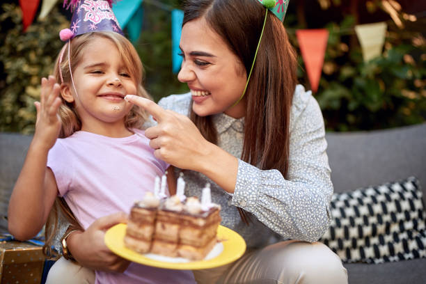 young female putting whipped cream from a birthday cake on a nose of a cute little girl young adult female putting whipped cream from a birthday cake on a nose of a cute little girl happy birthday cousin stock pictures, royalty-free photos & images