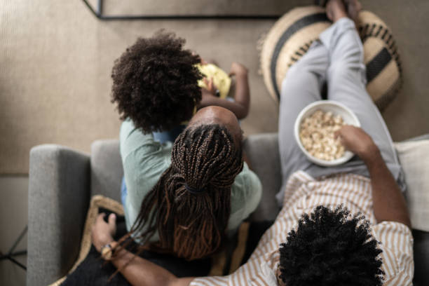 высокоугольный вид семьи едят попкорн и смотреть телевизор у себя дома - лёгкая закуска фотографии стоковые фото и изображения