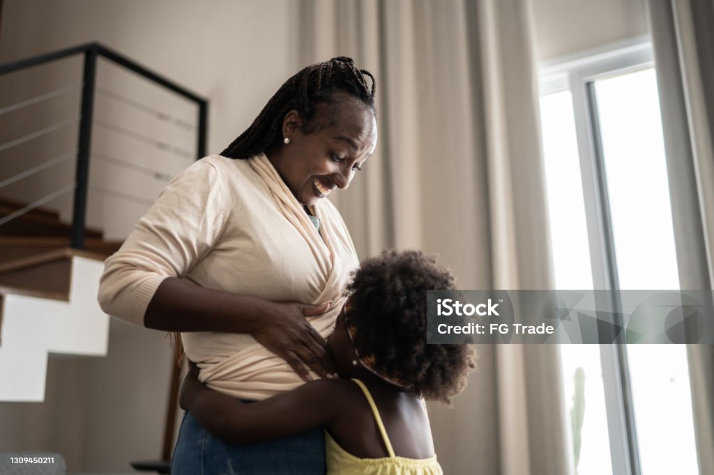 Girl kissing her pregnant mother's belly at home Pregnant Stock Photo