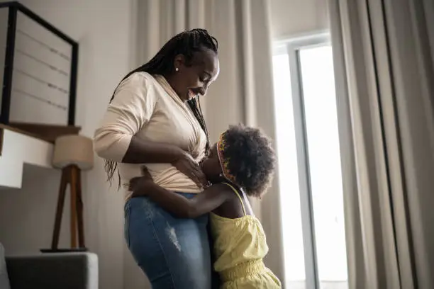 Photo of Girl kissing her pregnant mother's belly at home