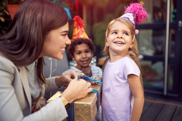 young female brunette opening  birthday presents to a little girl looking away. young female brunette opening  birthday presents to a little girl looking away, smiling happy birthday cousin stock pictures, royalty-free photos & images
