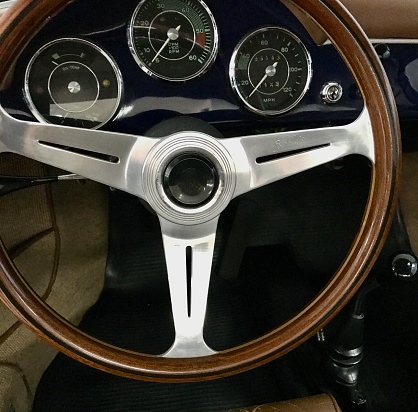 Classic British Jaguar E-type sports car in red. ( Also known as the Jaguar XK-E)\nInterior view of the dashboard and steering wheel of the vintage car.